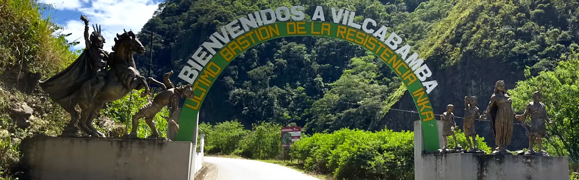 Arco de bienvenida a Vilcabamba, último bastión de la resistencia inca, rodeado de montañas verdes y esculturas de personajes incas