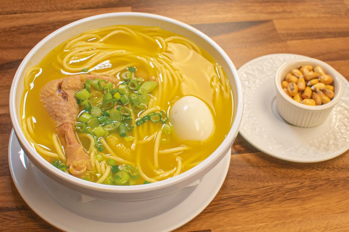 Caldo de gallina peruano con fideos, papa, huevo y cebolla china servido en un plato hondo