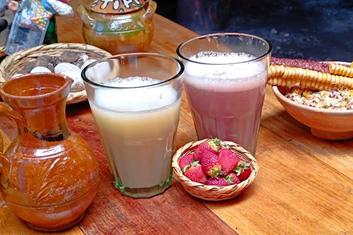 Vasos de chicha de jora y frutillada acompañados de una jarra de barro, fresas frescas y maíz sobre una mesa de madera