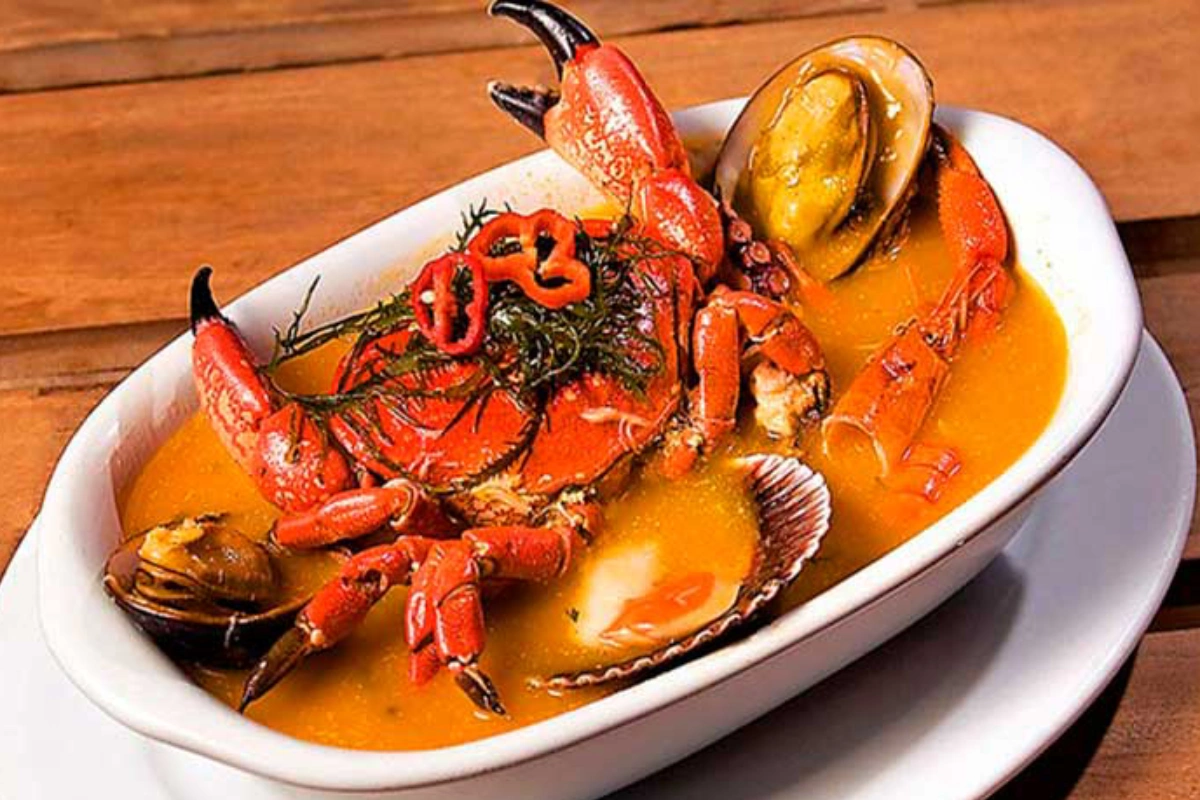 Parihuela con pescado y mariscos en caldo de ají, servida caliente con limón y culantro.
