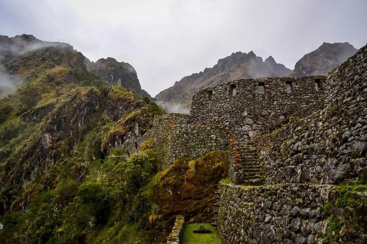 Escalinata de piedra entre muros incas de Sayacmarca con montañas y neblina al fondo